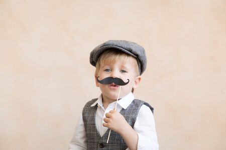 Funny kid holding fake mustache. Happy child playing in homeの写真素材