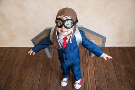 Portrait of young businessman with toy paper wings. Happy child playing at home. Kid having fun. Success, creative and start up conceptの写真素材