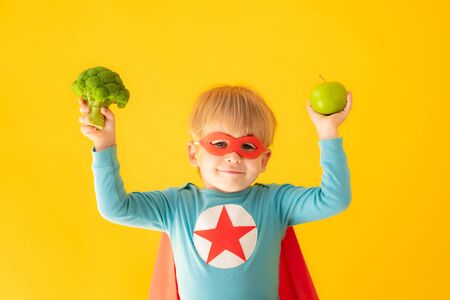 Superhero child holding broccoli and apple. Kid pretend to be super hero. Healthy eating conceptの写真素材