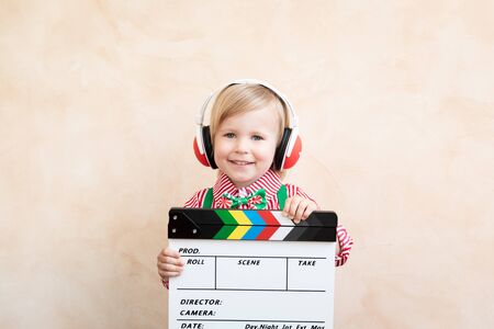 Funny kid holding clapper board. Happy child having fun at home. Retro cinema conceptの写真素材