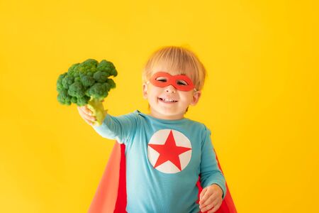 Superhero child holding broccoli. Kid pretend to be super hero. Healthy eating conceptの写真素材