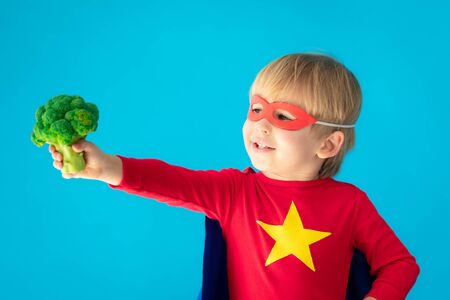 Superhero child holding broccoli. Kid pretend to be super hero. Healthy eating conceptの写真素材