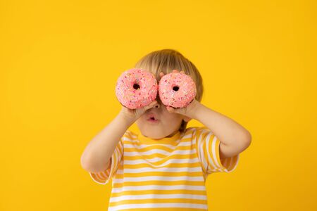 Happy child holding glazed donut. Portrait of funny kid against yellow backgroundの写真素材