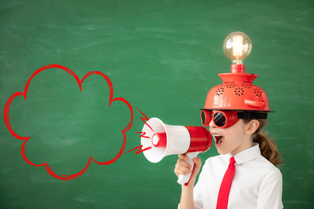 Happy child in classroom. Funny kid with light bulb against green chalkboard background. Innovation...