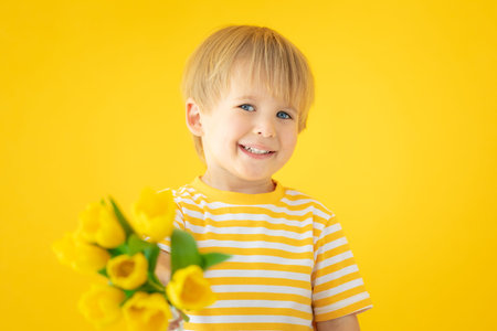 Happy child holding spring bouquet of flowers. Happy kid with tulips against yellow background. ....