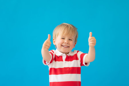 Close up portrait of happy child wearing striped shirt against blue background. Kid having fun on...