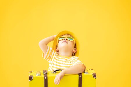 Portrait of happy child with suitcase against yellow background. Kid having fun on summer vacation. Dream and imagination conceptの写真素材