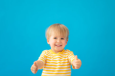 Close up portrait of happy child wearing striped shirt against blue background. Kid having fun on...