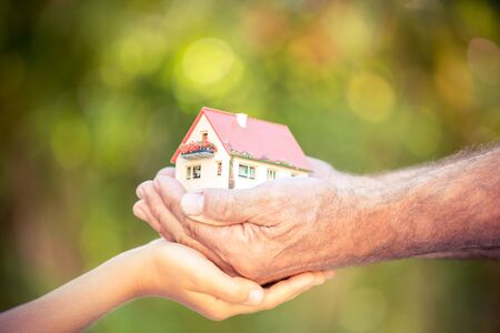 Senior man and child holding house in hands against spring green background. Real estate conceptの写真素材