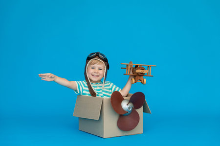 Happy child dreams of becoming a pilot. Kid having fun against blue paper background. Boy wearing...