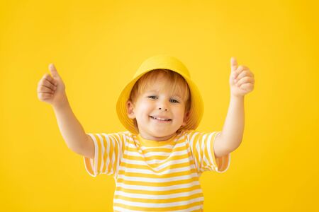 Portrait of happy child showing thumbs up against yellow background. Kid having fun on summer vacation. Dream and imagination conceptの写真素材