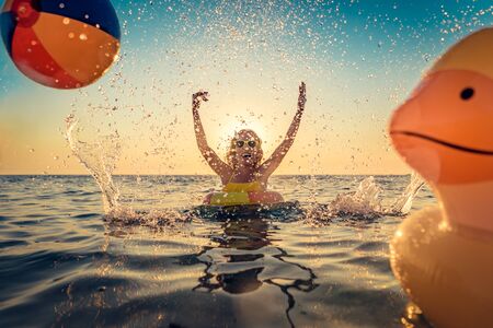 Happy child having fun on summer vacation. Kid playing with rubber duck and ball in the sea.の写真素材