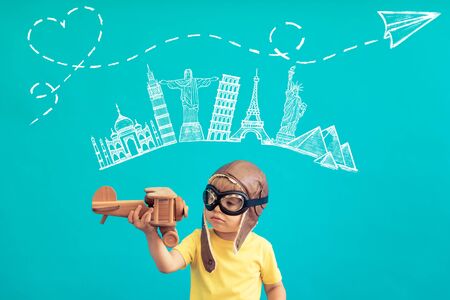 Happy child playing with vintage wooden airplane. Kid having fun against blue background. Imagination and freedom conceptの写真素材