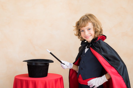 Child magician holding magic wand. Happy kid with top hat on table. Illusion and imagination conceptの写真素材
