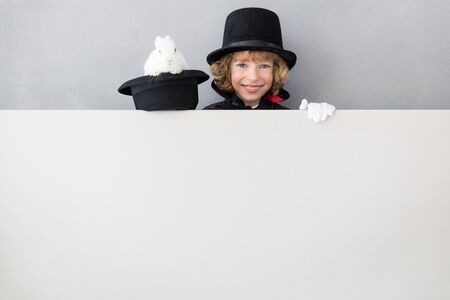Child magician with rabbit hiding behind banner blank. Happy kid holding cardboard background with copy spaceの写真素材