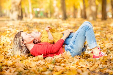 Happy family having fun outdoor in autumn park. Mother and child against yellow blurred leaves backgroundの写真素材