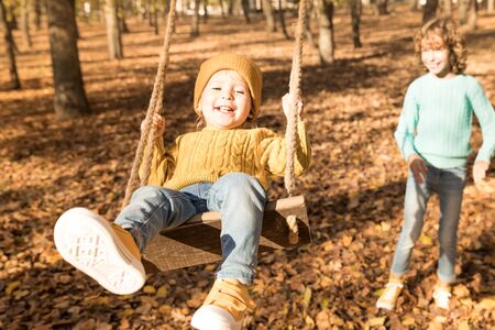 Happy children having fun outdoor in autumn park. Kids playing on swing against yellow blurred leaves background. Freedom and carefree conceptの写真素材