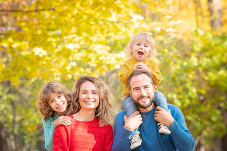 Happy family having fun outdoor in autumn park. Children and parents against yellow blurred leaves backgroundの写真素材