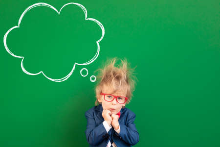 Afraid child student in class. Sad kid against green chalkboard. Online education and e-learning concept. Back to schoolの写真素材
