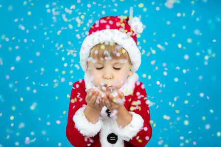 Happy child wearing Santa Claus costume. Kid blowing confetti against blue background. Christmas holiday conceptの写真素材
