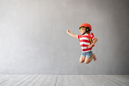Child with rocket jumping against grey concrete background. Kid playing at home. Childhood dream and...