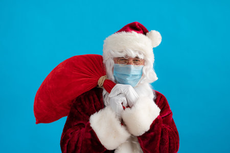 Senior wearing Santa Claus costume and protective mask. Man holding bag with gifts. Christmas...