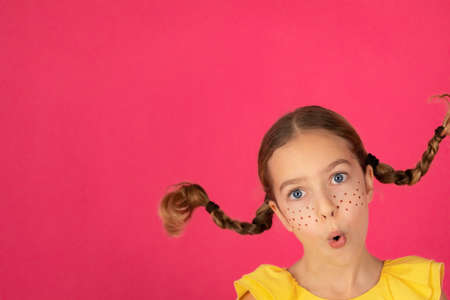 Surprised girl against pink background. Portrait of funny childの写真素材