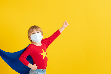 Superhero child playing indoor. Portrait of super hero kid against yellow paper background. Stop coronavirus COVID-19 pandemic conceptの写真素材