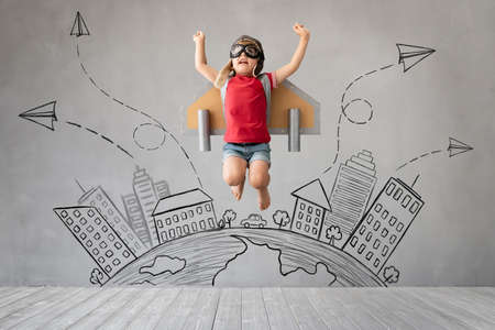 Child with jetpack jumping against grey concrete background. Kid with jet pack playing at home. Childhood dream and freedom conceptの写真素材