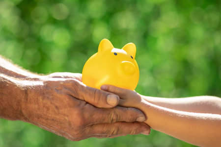 Family holding piggy bank in hands against green spring background. Fundraiser for environmental protection conceptの写真素材