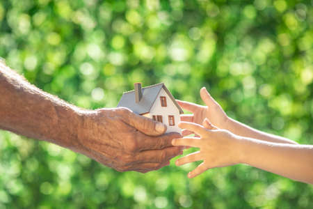 Family holding eco house in hands against spring green background. Real estate and Earth day holiday conceptの写真素材