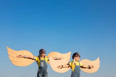 Happy children playing with toy wings against summer sky background. Kids having fun outdoor. Imagination and dream conceptの写真素材