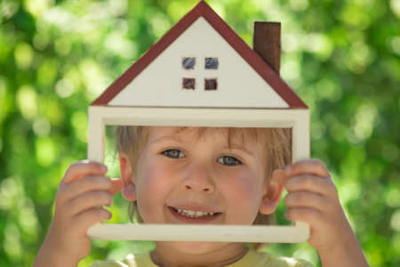 Child holding eco house in hands against spring green background. Real estate and Earth day holiday conceptの写真素材
