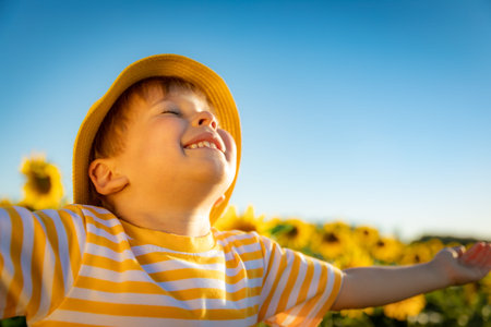 Happy child playing with sunflower outdoor. Kid having fun in green spring field against blue sky background. Healthy and active lifestyle conceptの写真素材