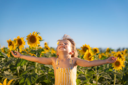 Happy child playing with sunflower outdoor. Kid having fun in green spring field against blue sky background. Healthy and active lifestyle conceptの写真素材