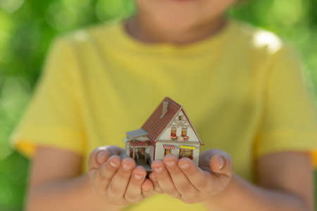 Child holding eco house in hands against spring green background. Real estate and Earth day holiday conceptの写真素材