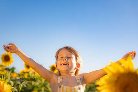 Happy child playing with sunflower outdoor. Kid having fun in green spring field against blue sky background. Healthy and active lifestyle conceptの写真素材