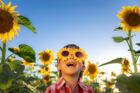 Happy child playing with sunflower outdoor. Kid having fun in green spring field against blue sky background. Healthy and active lifestyle conceptの写真素材