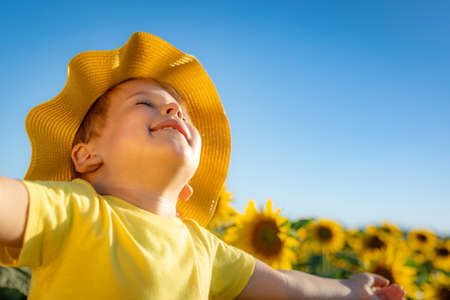 Happy child playing with sunflower outdoor. Kid having fun in green spring field against blue sky background. Healthy and active lifestyle conceptの写真素材