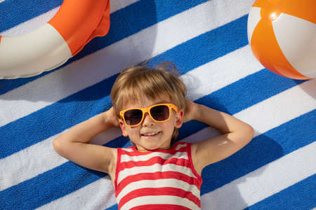 Happy child lying on striped towel outdoor. Top view portrait of kid. Funny baby smiling. Summer vacation conceptの写真素材