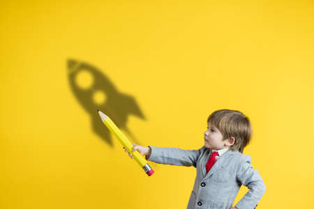 Happy child holding pencil against yellow background. Business start up and education conceptの写真素材