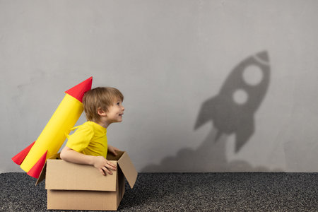 Happy child with toy paper rocket wants to fly. Funny kid dreams about space. Imagination, freedom and motivation conceptの写真素材