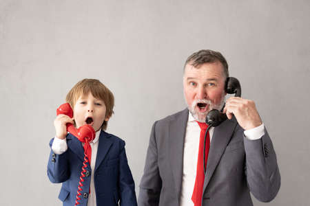 Funny child and senior man pretend to be businessmen. Grandfather and kid playing at home. Education, start up and business idea conceptの写真素材