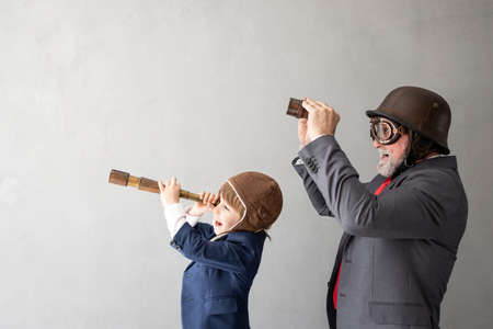 Funny child and senior man pretend to be businessmen. Grandfather and kid playing at home. Education, start up and business idea conceptの写真素材
