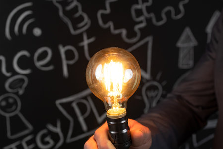 Businessman holding lightbulb in hand against blackboard