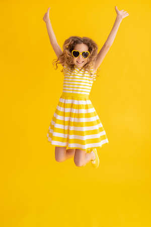 Happy child jumping against yellow summer background. Portrait of cheerful girl. Success and winner conceptの写真素材