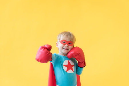 Portrait of superhero child. Super hero kid against yellow paper background. Happy child wearing red mask and cape of superhero. Children dream and imagination conceptの写真素材
