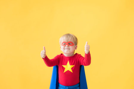 Portrait of superhero child. Super hero kid against yellow paper background. Happy child wearing red mask and cape of superhero. Children dream and imagination conceptの写真素材