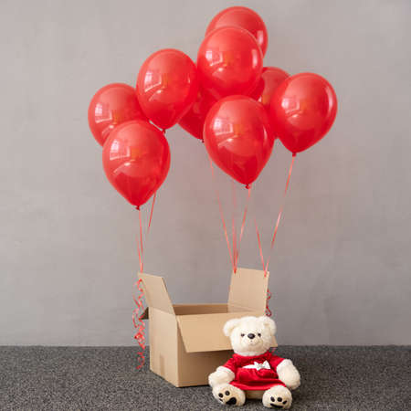 Teddy bear wearing Christmas costume near box with red balloons. Xmas holiday conceptの写真素材