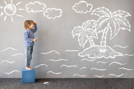 Dream big! Happy child playing outdoor. Funny kid draws a chalk sea on the wall. Child dreams about travel. Kid pretend to be captain. Children imagination and summer vacation conceptの写真素材